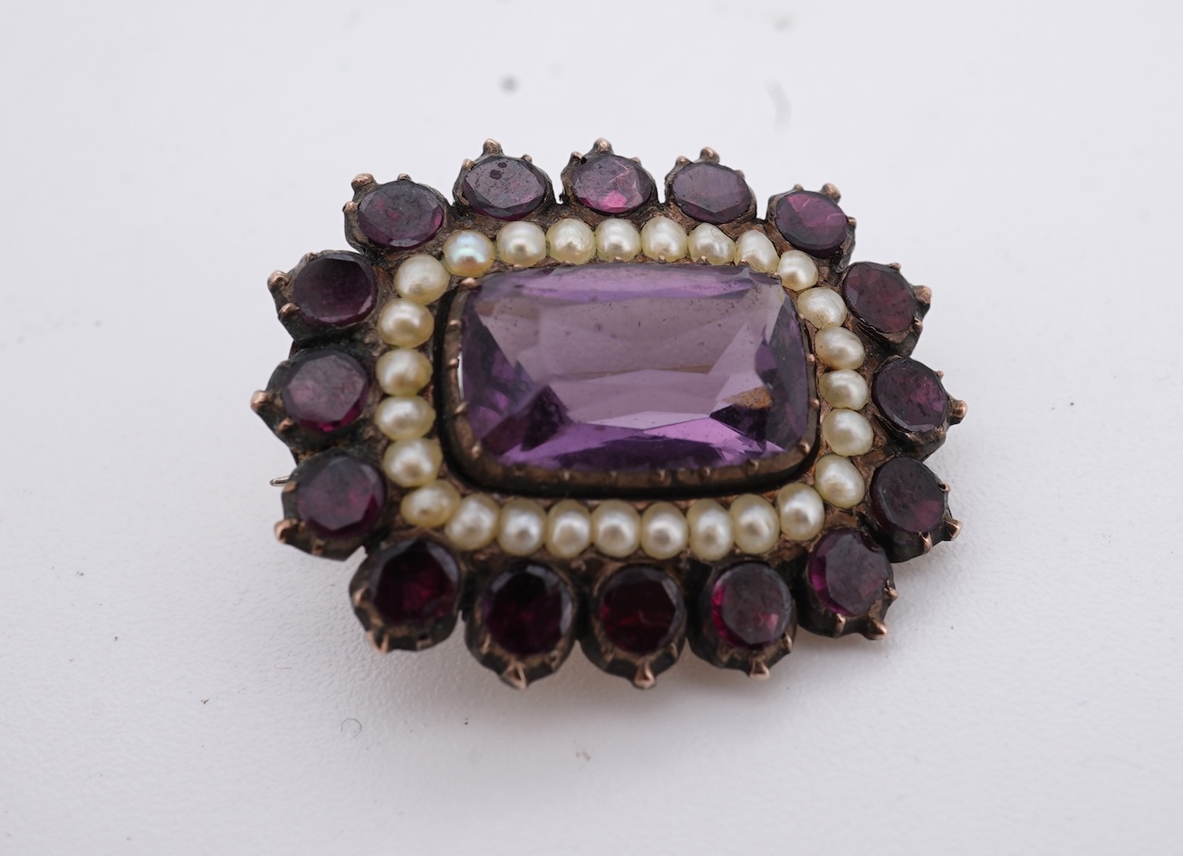 A Victorian yellow metal, amethyst and garnet cluster set brooch, 22mm, an early 20th century yellow metal and seed pearl set heart shaped locket, a yellow metal, garnet and zircon set three stone bar brooch and a tortoi